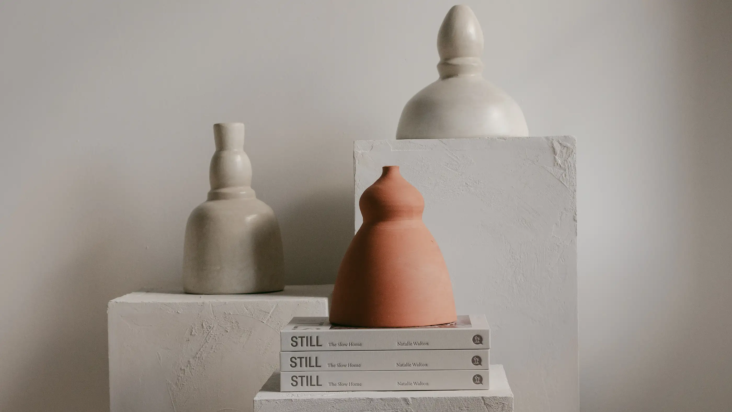 Ochre and Silk product styling — stoneware vessels in cream and terracotta on a plaster plinth