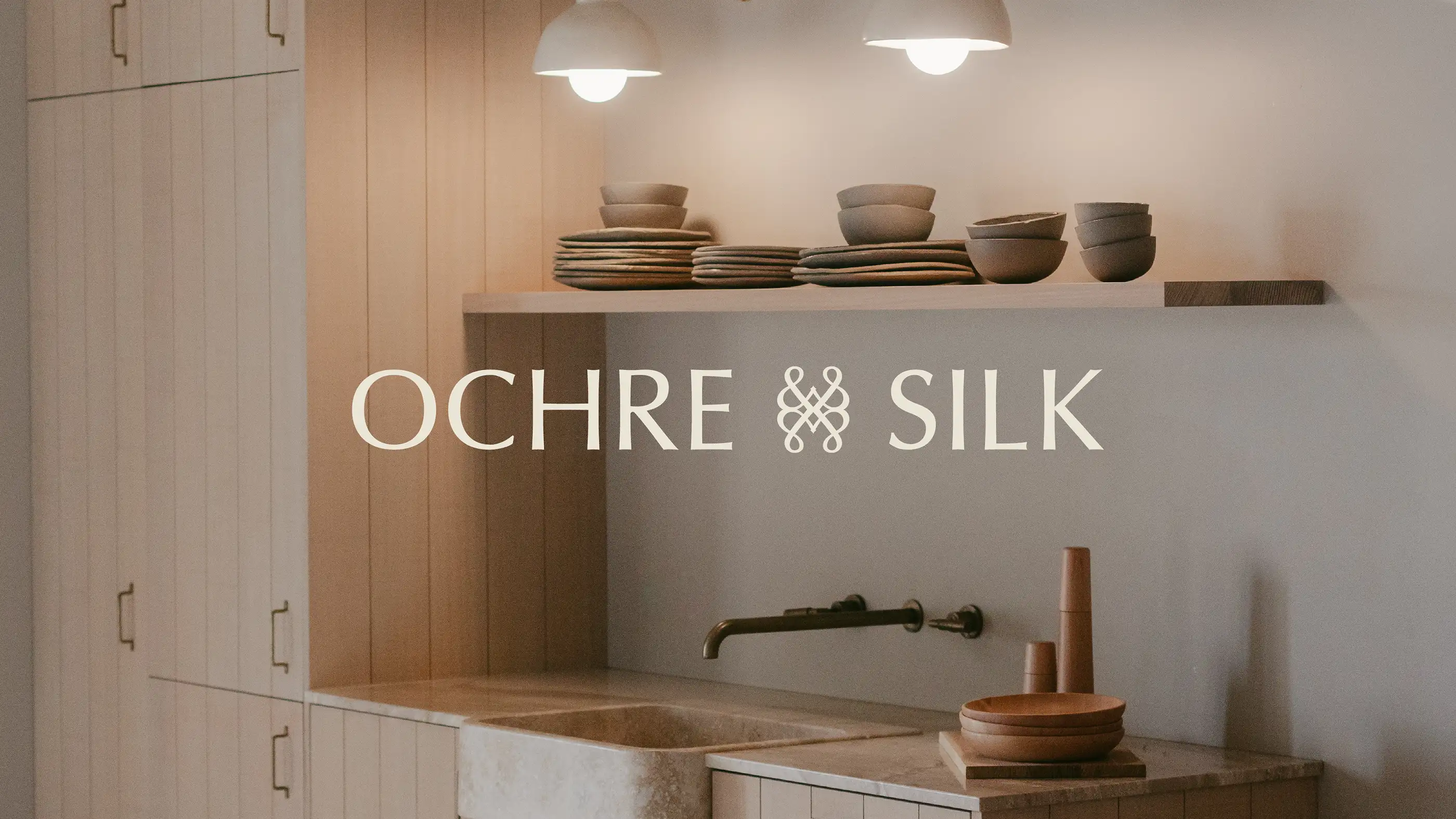 Ochre and Silk logotype over a pale timber kitchen with stoneware bowls on an open shelf