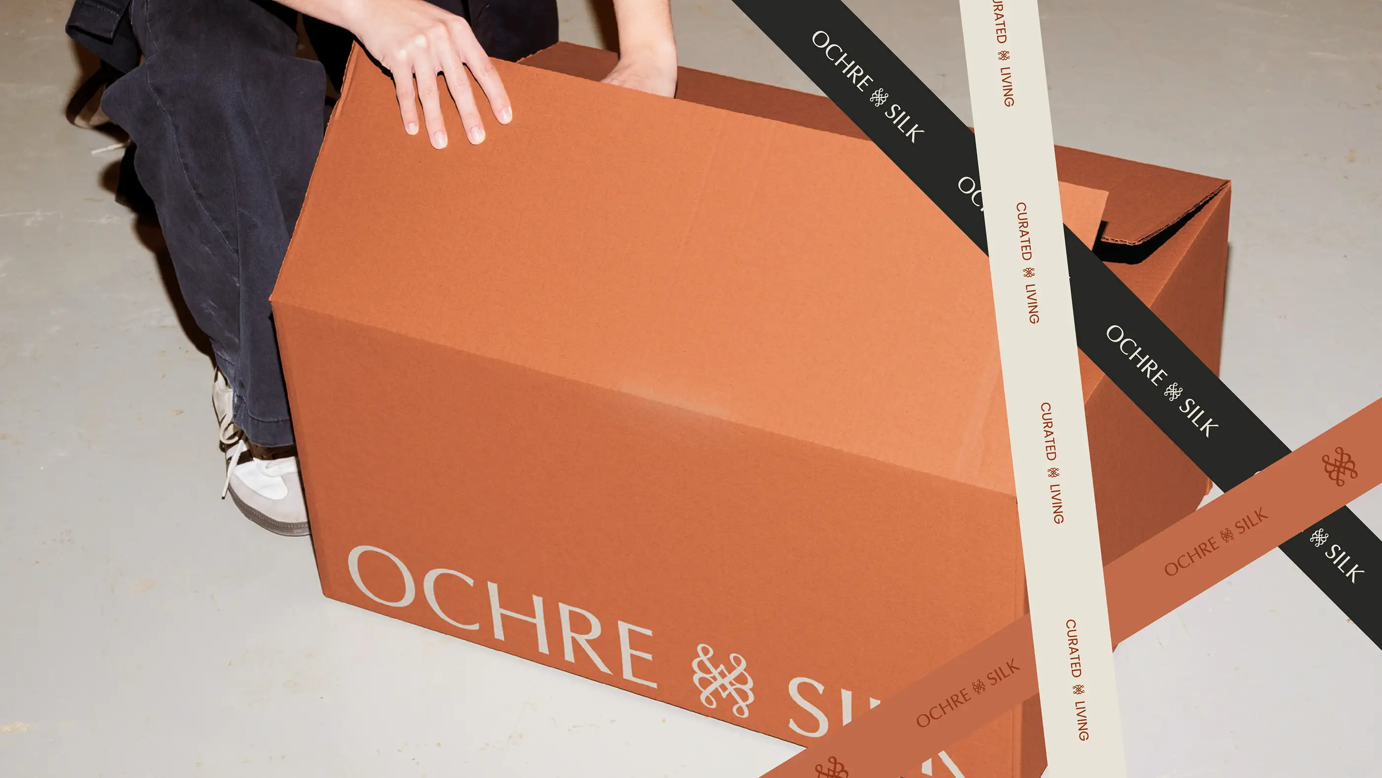 Ochre and Silk delivery box in terracotta being taped closed with branded ribbon