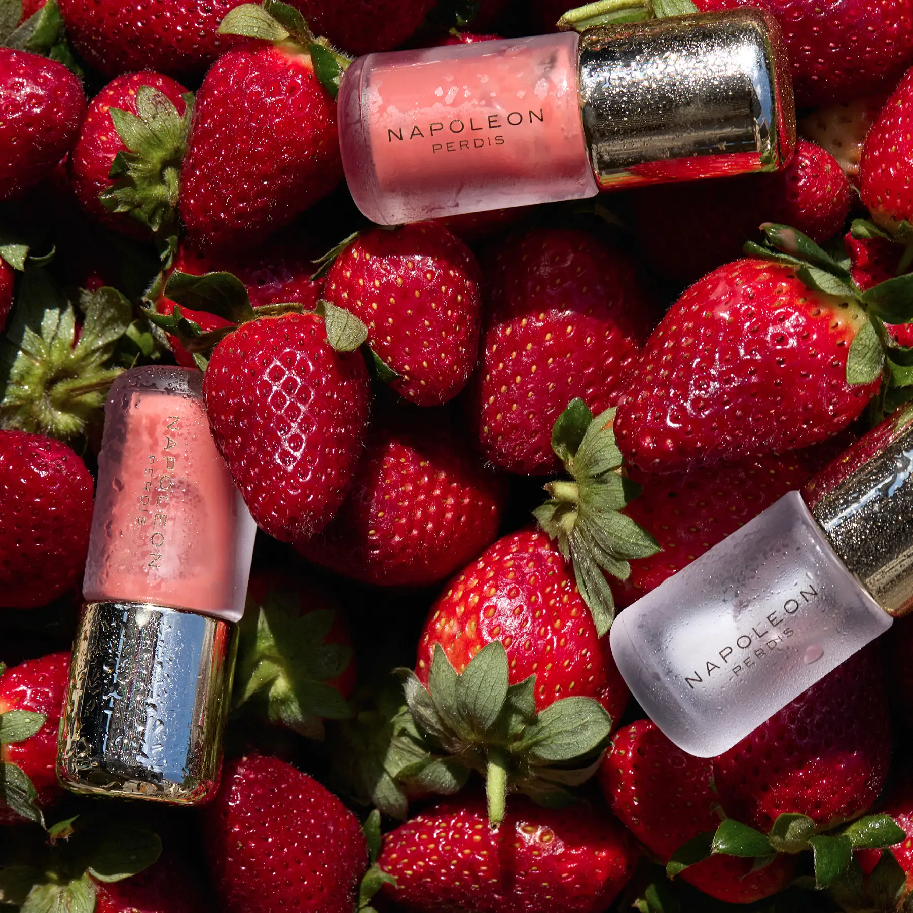 Napoleon Perdis lip glosses scattered across fresh strawberries