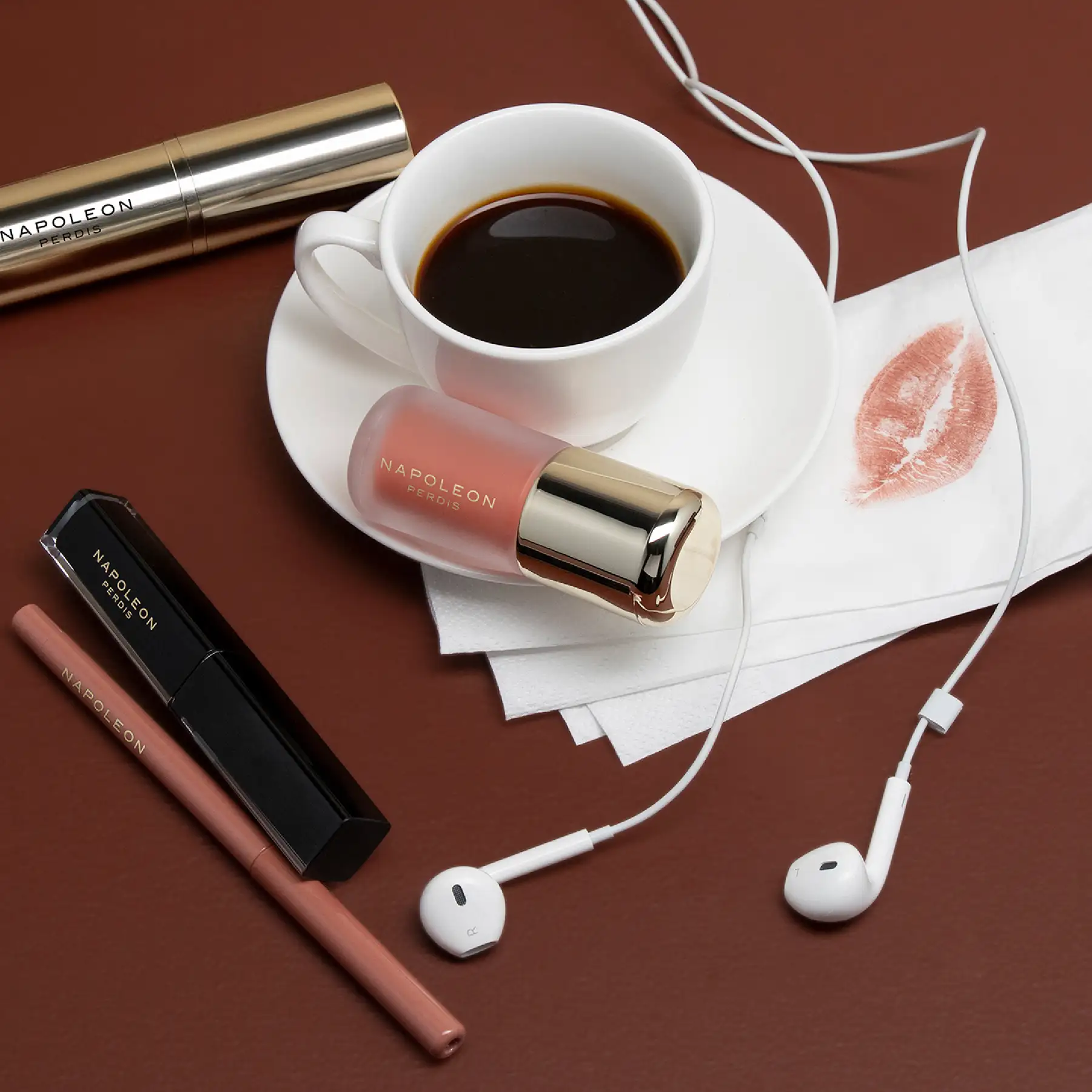 Napoleon Perdis lip products styled with an espresso cup, a lipstick print on a napkin and earphones