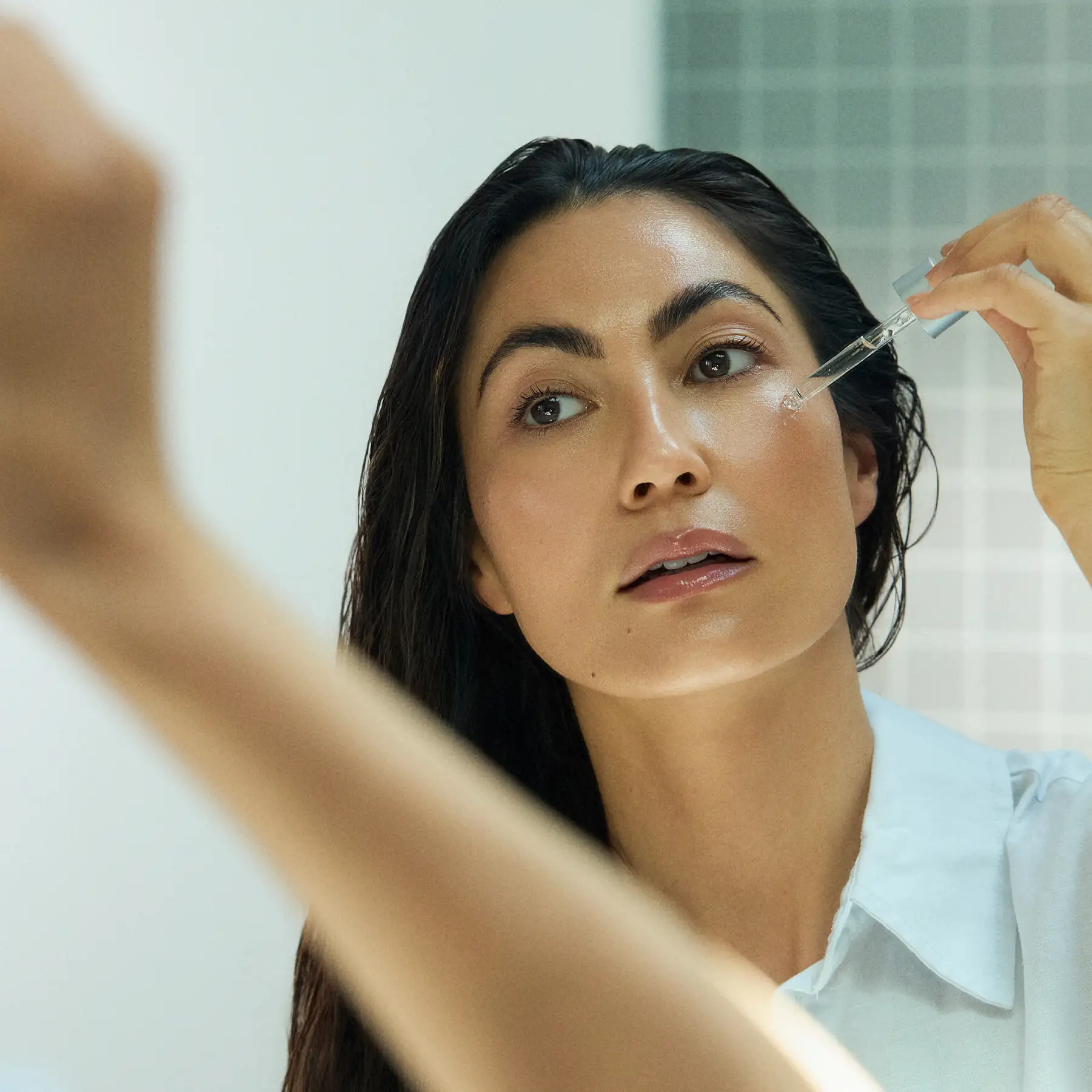 Napoleon Perdis campaign photography — model applying serum with a dropper at a mirror
