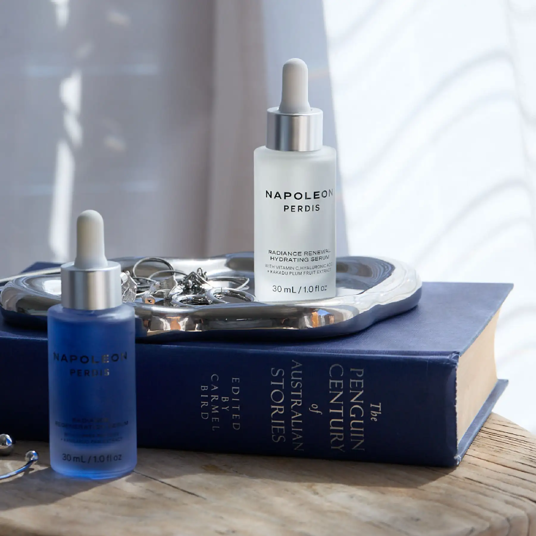 Napoleon Perdis serums styled on a silver tray beside a book of Australian stories