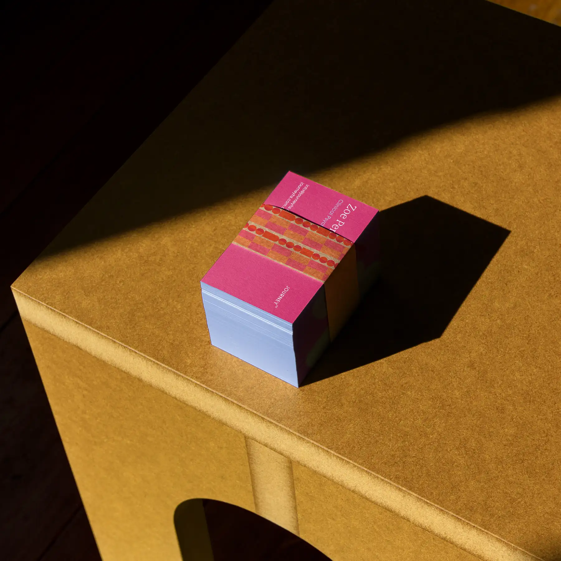 Stack of Journey HS business cards with pink edge-printing, on a cardboard box